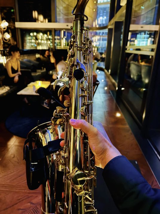 Cây kèn saxophone trong không gian lounge với ánh sáng ấm và quầy bar phía sau